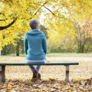 A lady sitting on a park bench with autumn leaves behind her.