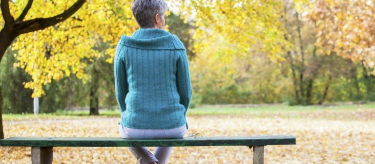 A lady sitting on a park bench with autumn leaves behind her.