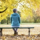 A lady sitting on a park bench with autumn leaves behind her.