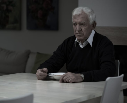 An older man sitting at a table and eating by himself while he stares into space