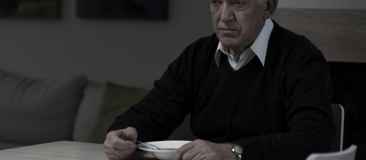 An older man sitting at a table and eating by himself while he stares into space