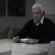 An older man sitting at a table and eating by himself while he stares into space