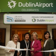 Four ladies stand cutting a ribbon to mark the opening of the Irish Travel Trade Show Dublin with a banner behind announcing Dublin Airport as sponsors of the event.