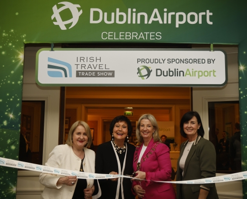 Four ladies stand cutting a ribbon to mark the opening of the Irish Travel Trade Show Dublin with a banner behind announcing Dublin Airport as sponsors of the event.