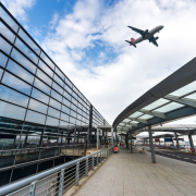 A glass building that is an airport and in the background a plan flying over