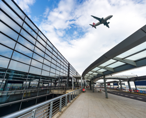 A glass building that is an airport and in the background a plan flying over