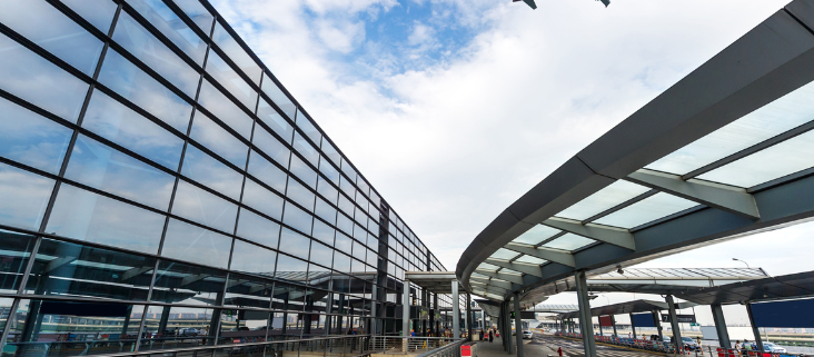 A glass building that is an airport and in the background a plan flying over