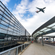 A glass building that is an airport and in the background a plan flying over
