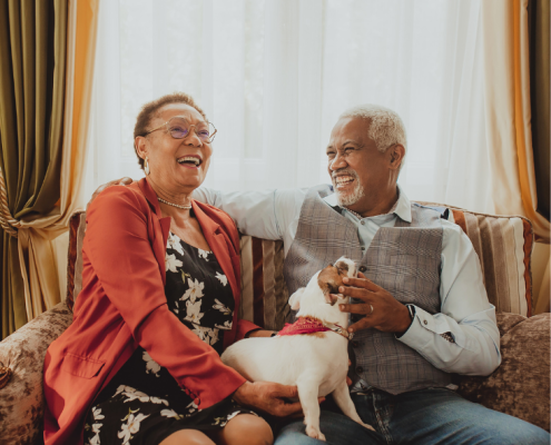 An older couple sitting on a couch with a dog.