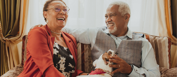 An older couple sitting on a couch with a dog.