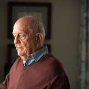 Older man in red sweater looking out a window.