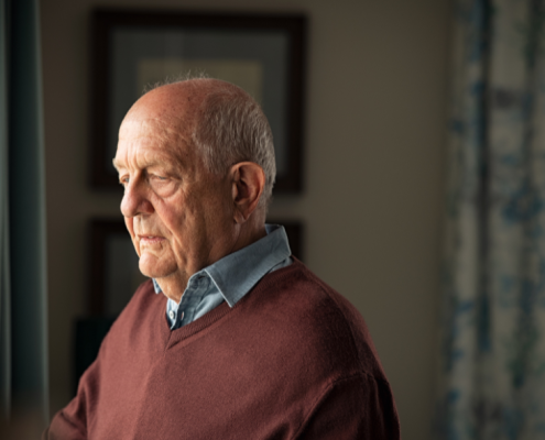 Older man in red sweater looking out a window.