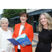 Three women standing next to each other. Person in the middle is holding a book.