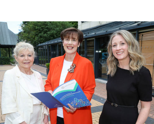 Three women standing next to each other. Person in the middle is holding a book.